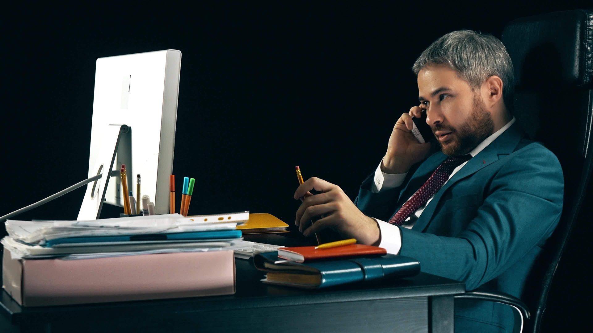 Bearded businessman talking on his cell phone. Dark background, isolated