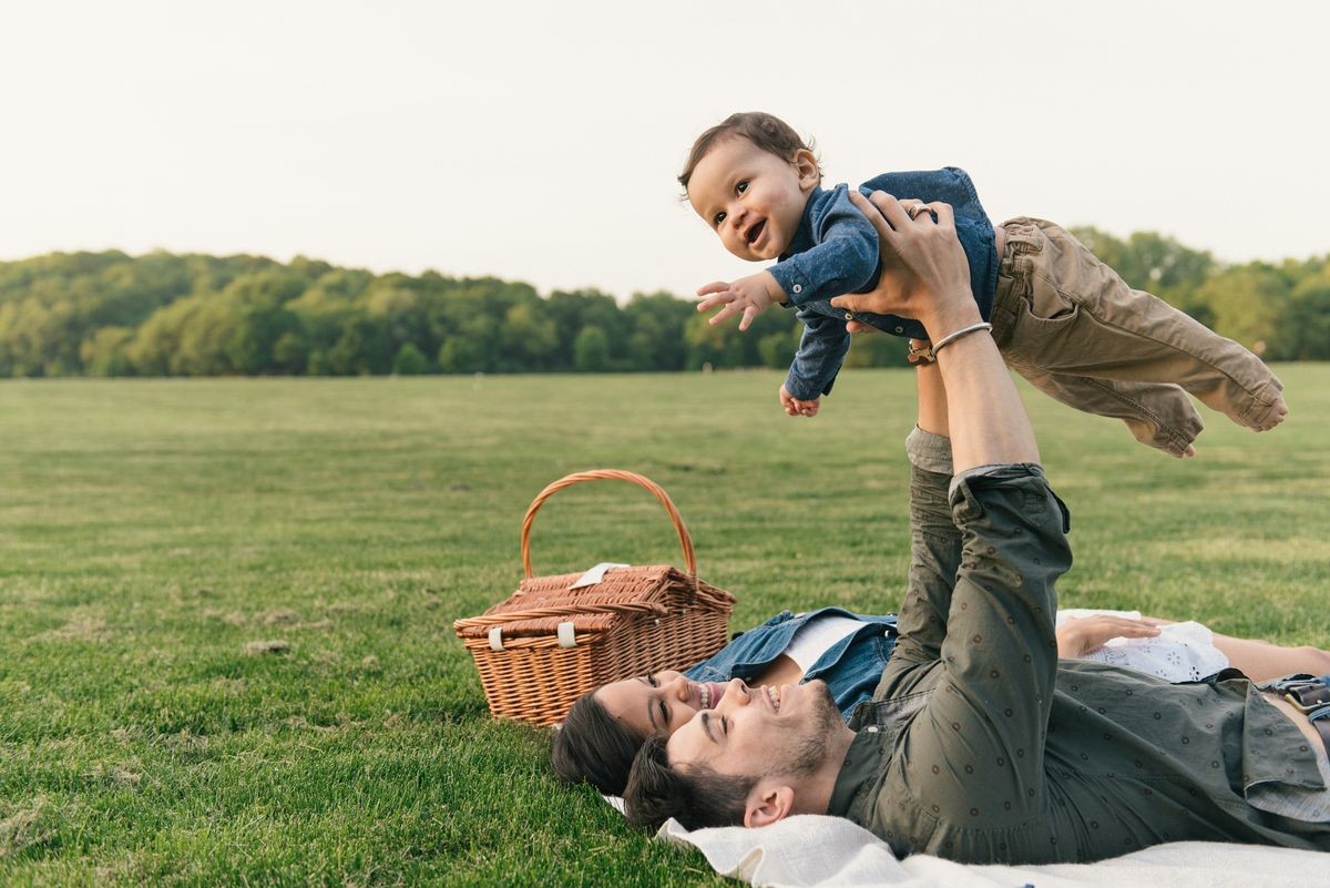 Mother and father laying on backs raising baby boy into the air